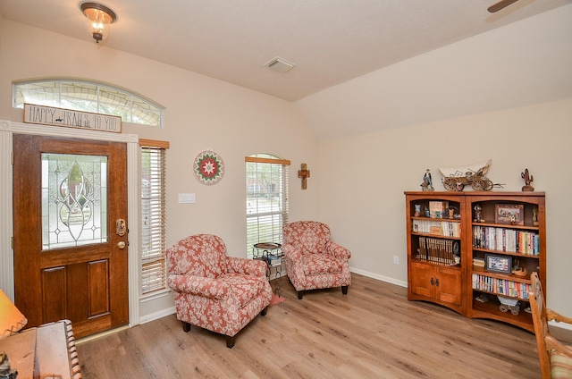 living area featuring lofted ceiling, light wood finished floors, visible vents, and baseboards