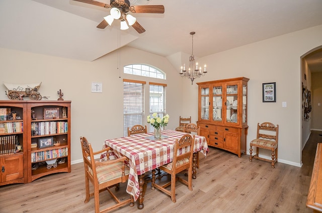 dining room with arched walkways, lofted ceiling, ceiling fan with notable chandelier, baseboards, and light wood-style floors