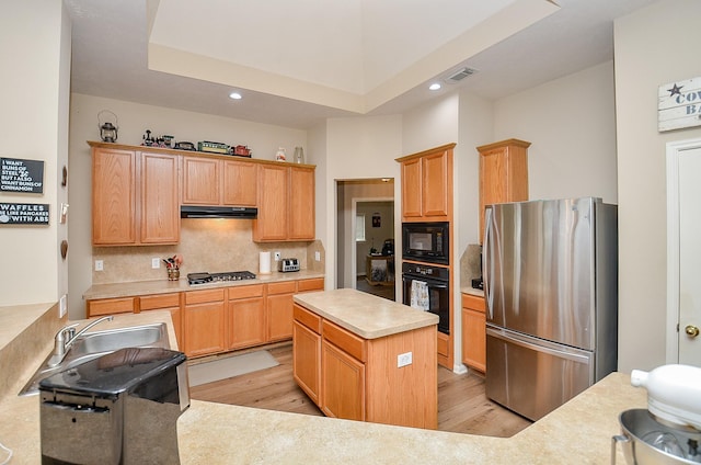 kitchen featuring tasteful backsplash, light countertops, light wood-type flooring, under cabinet range hood, and black appliances