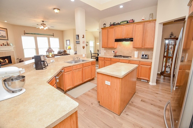 kitchen featuring a tiled fireplace, open floor plan, light countertops, under cabinet range hood, and a sink