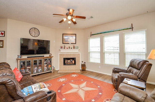 living area with baseboards, visible vents, a tiled fireplace, and wood finished floors