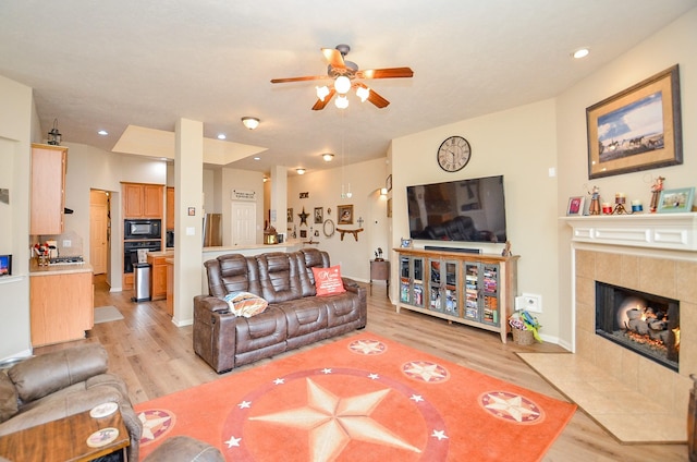 living room with light wood finished floors, a tiled fireplace, a ceiling fan, and baseboards