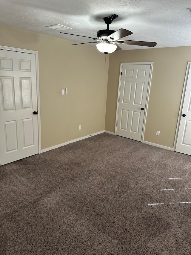 spare room featuring a textured ceiling, dark colored carpet, and baseboards