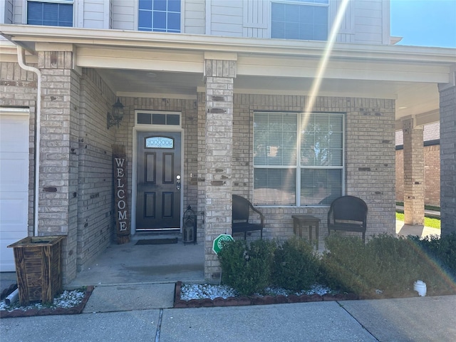 entrance to property with a garage, a porch, and brick siding