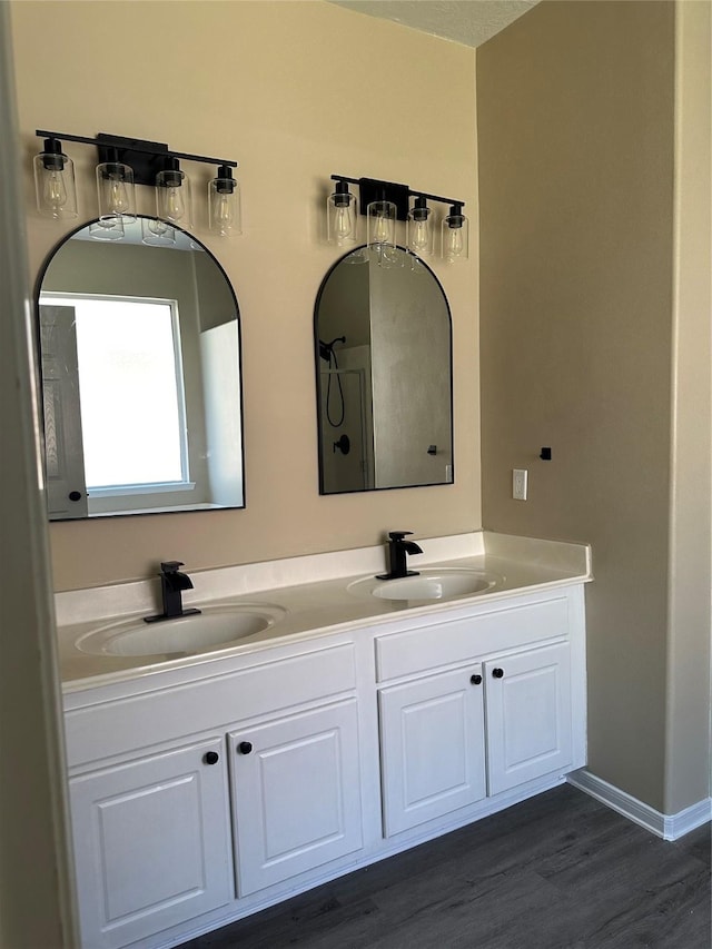 bathroom with double vanity, wood finished floors, a sink, and baseboards