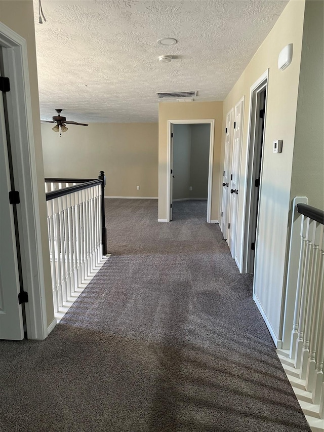 corridor with visible vents, baseboards, an upstairs landing, a textured ceiling, and carpet flooring