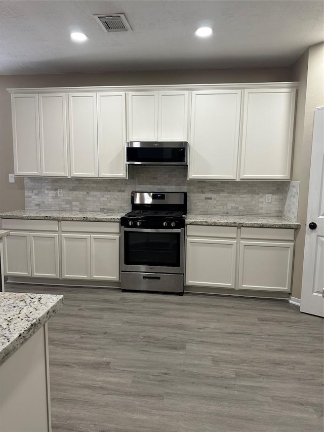 kitchen featuring stainless steel appliances, white cabinets, visible vents, and light wood-style floors