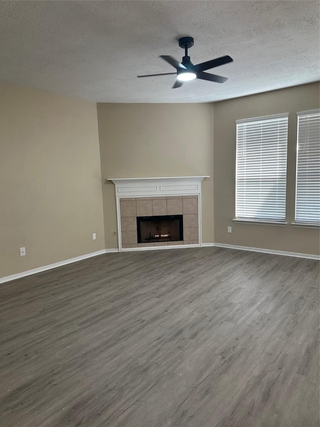 unfurnished living room with a fireplace, a textured ceiling, baseboards, and wood finished floors