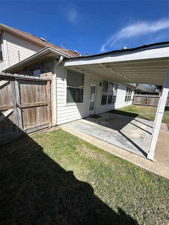 back of house featuring a carport, a patio area, fence, and a lawn