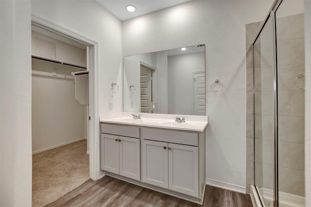 full bathroom with wood finished floors, a sink, a spacious closet, double vanity, and a stall shower