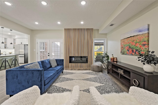 living room with french doors, recessed lighting, a glass covered fireplace, a textured ceiling, and wood finished floors