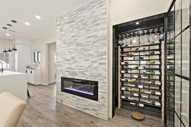 wine area with electric panel, wood finished floors, a textured ceiling, a fireplace, and recessed lighting