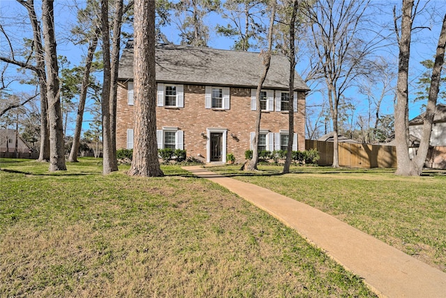 colonial-style house featuring a front lawn, fence, and brick siding