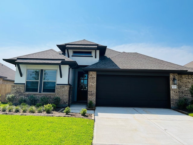 prairie-style house with an attached garage, brick siding, driveway, and roof with shingles