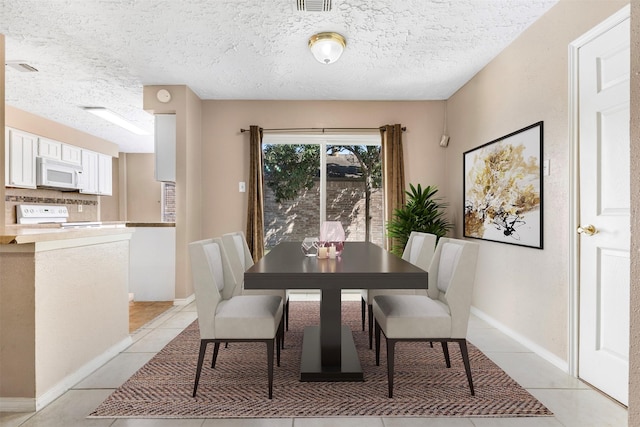 dining area with a textured ceiling, light tile patterned flooring, visible vents, and baseboards