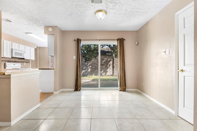 unfurnished dining area with a textured ceiling, light tile patterned flooring, visible vents, and baseboards