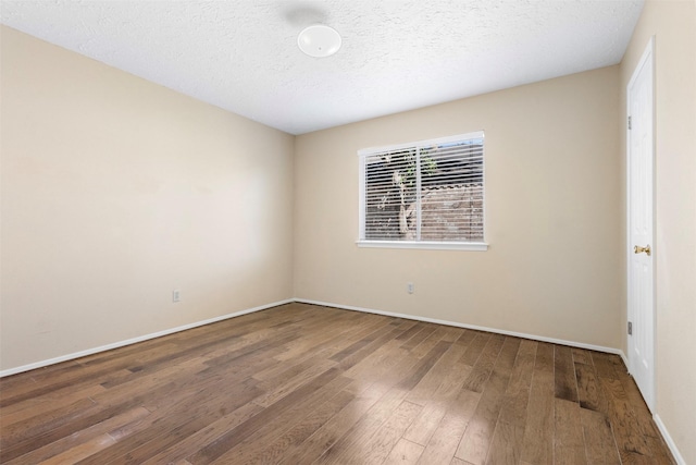 spare room with a textured ceiling, baseboards, and wood finished floors