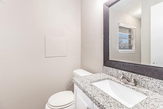 half bathroom featuring toilet, a textured wall, and vanity