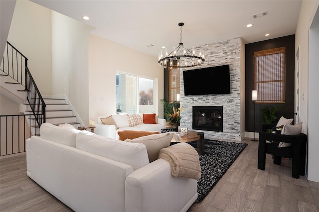 living room featuring an inviting chandelier, stairs, light wood-type flooring, a fireplace, and recessed lighting