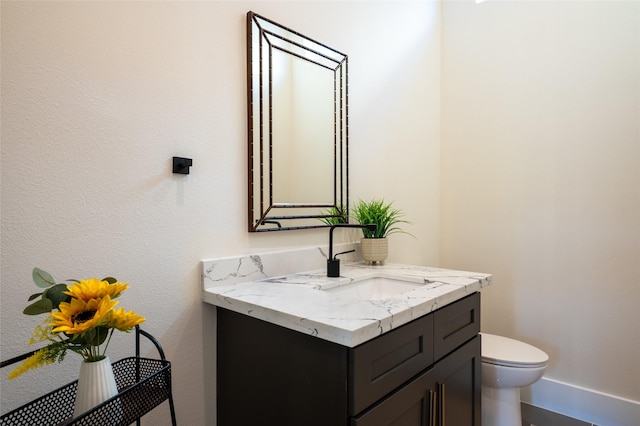 half bath with toilet, baseboards, and vanity