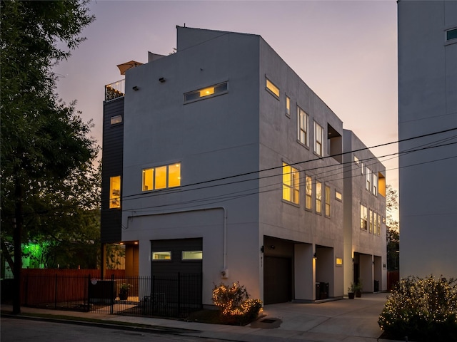 back of property at dusk featuring a garage, fence, driveway, and stucco siding