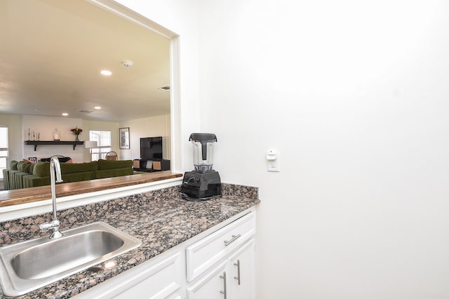 kitchen featuring recessed lighting, a sink, white cabinets, open floor plan, and dark stone countertops