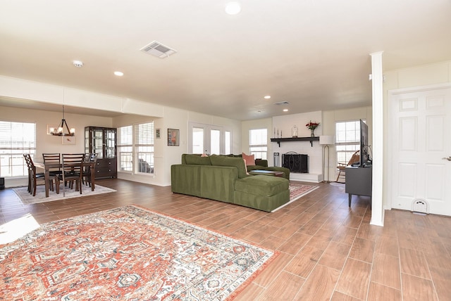 living area featuring a fireplace with raised hearth, a notable chandelier, wood finish floors, visible vents, and french doors