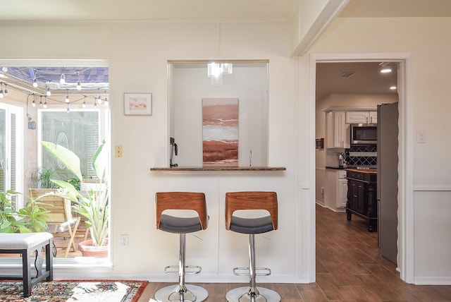 kitchen featuring dark wood-style floors, stainless steel microwave, backsplash, and visible vents