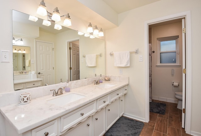 bathroom featuring double vanity, a sink, toilet, and baseboards