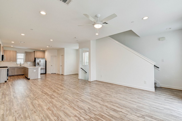 unfurnished living room featuring baseboards, light wood-type flooring, visible vents, and a healthy amount of sunlight