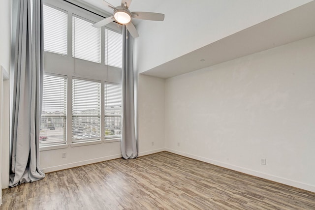 empty room featuring a ceiling fan, a high ceiling, baseboards, and wood finished floors