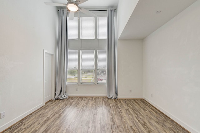 spare room featuring a ceiling fan, a high ceiling, baseboards, and wood finished floors