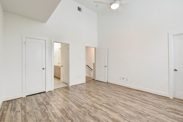 unfurnished bedroom featuring high vaulted ceiling, connected bathroom, light wood-style flooring, visible vents, and baseboards