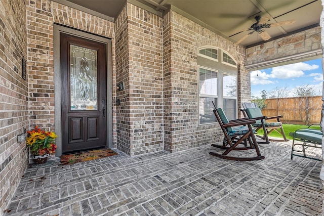 doorway to property with a ceiling fan, fence, and brick siding