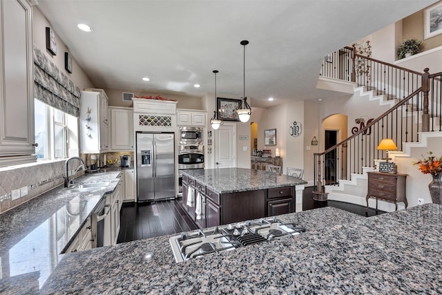 kitchen with arched walkways, a sink, decorative backsplash, dark wood-type flooring, and appliances with stainless steel finishes