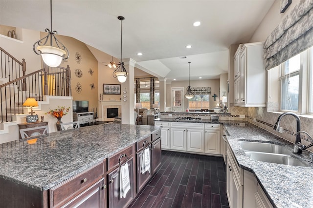 kitchen with wood finish floors, a sink, backsplash, white cabinetry, and a fireplace