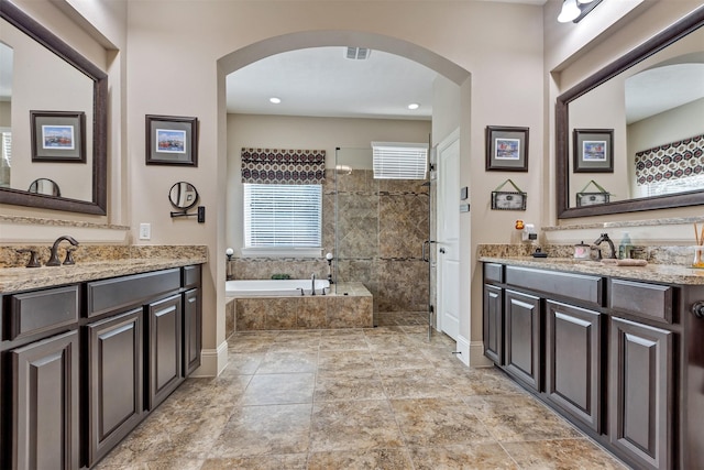 full bathroom featuring visible vents, a garden tub, two vanities, a tile shower, and a sink