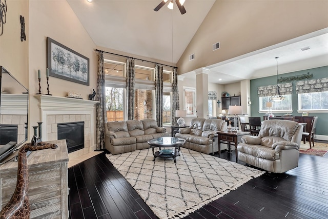 living room with visible vents, high vaulted ceiling, a tiled fireplace, decorative columns, and dark wood-style flooring