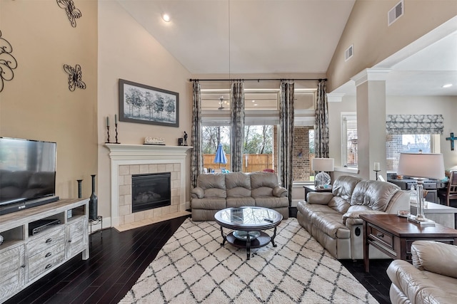 living area featuring dark wood finished floors, visible vents, a tiled fireplace, and high vaulted ceiling