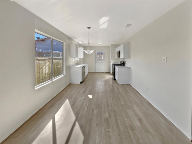 unfurnished dining area with light wood-type flooring, a sink, and visible vents