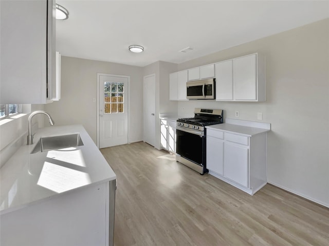 kitchen featuring appliances with stainless steel finishes, light countertops, a sink, and light wood-style flooring