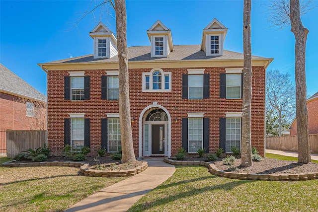 georgian-style home with brick siding, a front yard, and fence