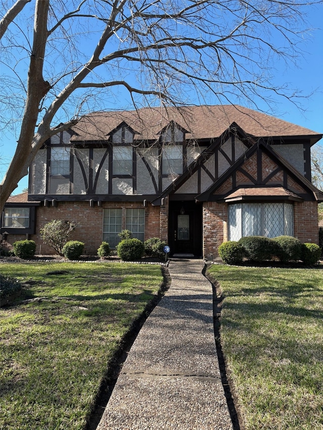 tudor-style house featuring brick siding and a front yard