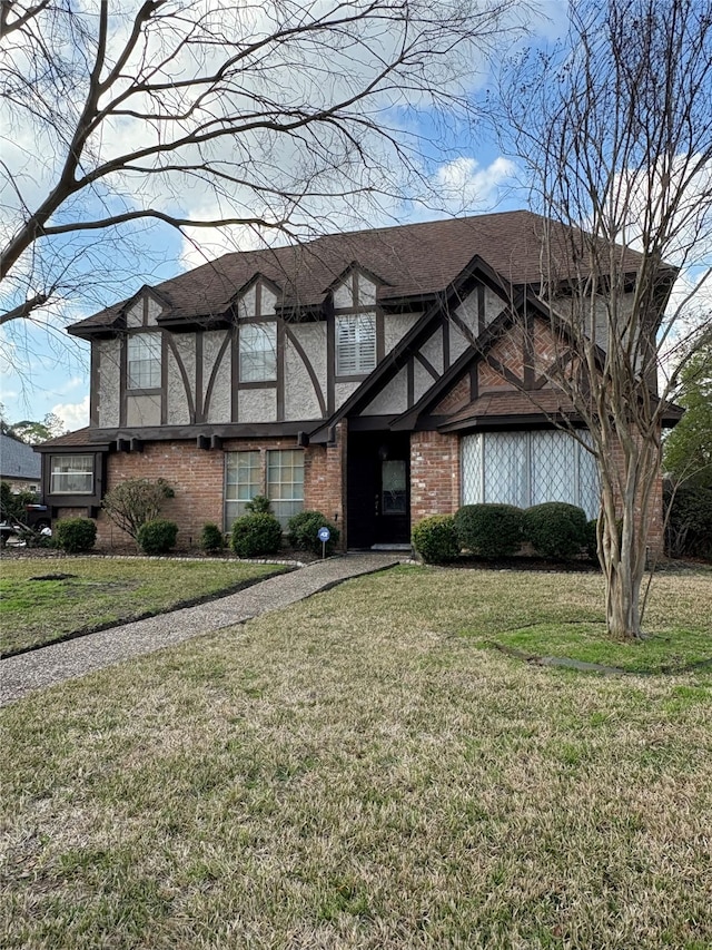 tudor house featuring brick siding, a shingled roof, and a front yard