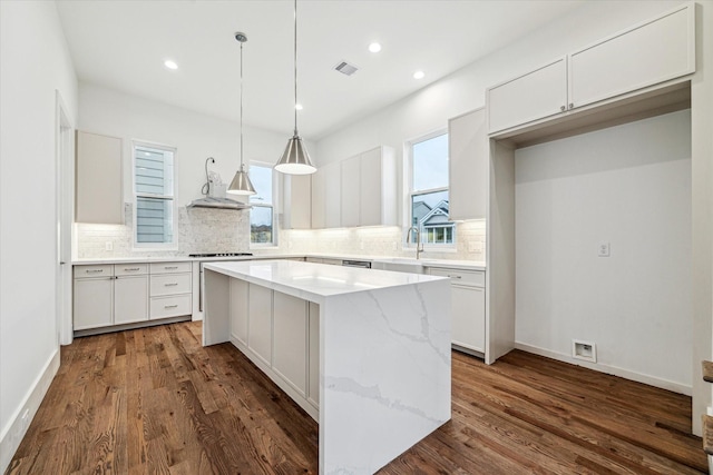 kitchen with wall chimney range hood, white cabinetry, visible vents, and a center island