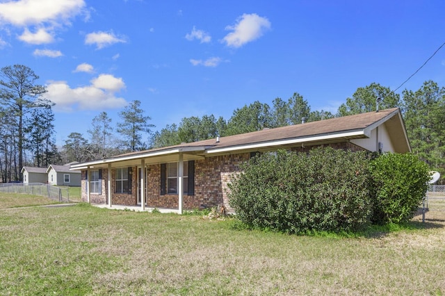 ranch-style house featuring a porch, a front yard, brick siding, and fence