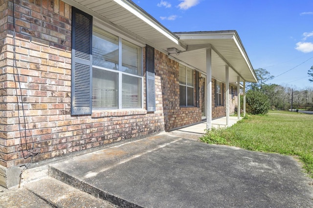 view of side of property with covered porch, brick siding, and a lawn