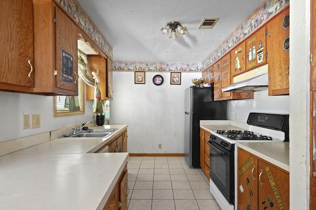 kitchen featuring under cabinet range hood, a sink, light countertops, brown cabinets, and range with gas cooktop