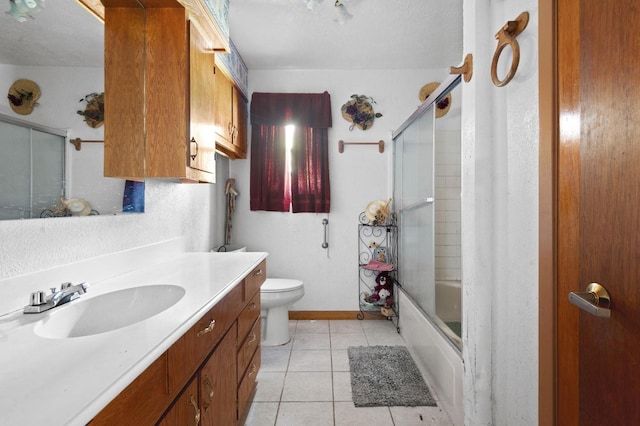 bathroom featuring toilet, enclosed tub / shower combo, vanity, tile patterned flooring, and baseboards