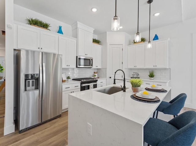 kitchen with a breakfast bar area, stainless steel appliances, a sink, white cabinets, and pendant lighting